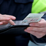 Инспектор ГАИ держит в руках водительское удостоверение и проверяет его подлинность.