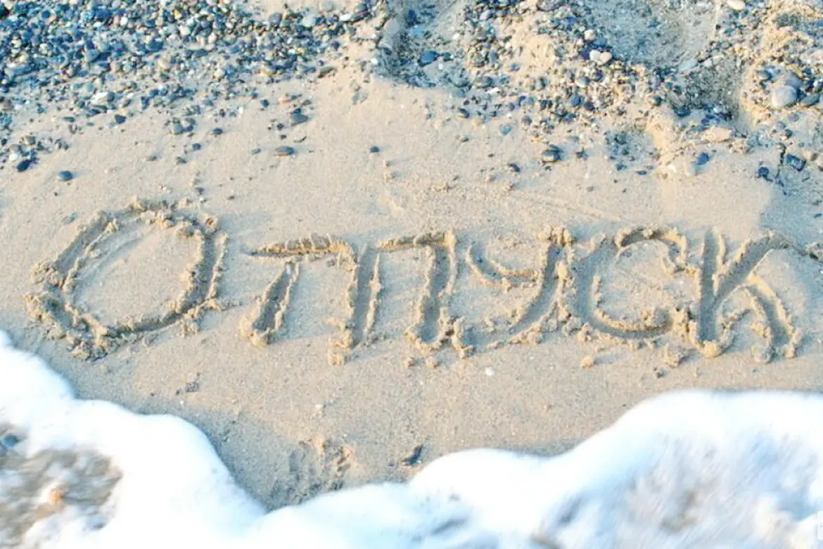 Надпись «отпуск», сделанная на песке у моря, которую частично смывает прибой.