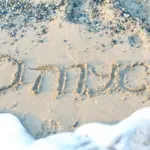 Надпись «отпуск», сделанная на песке у моря, которую частично смывает прибой.