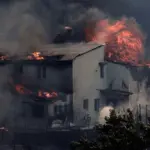 Горящий жилой дом, охваченный огнём и дымом во время лесных пожаров в пригороде Афин