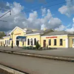 Здание железнодорожного вокзала в Осиповичах на фоне облачного неба, видны платформы и контактные линии.