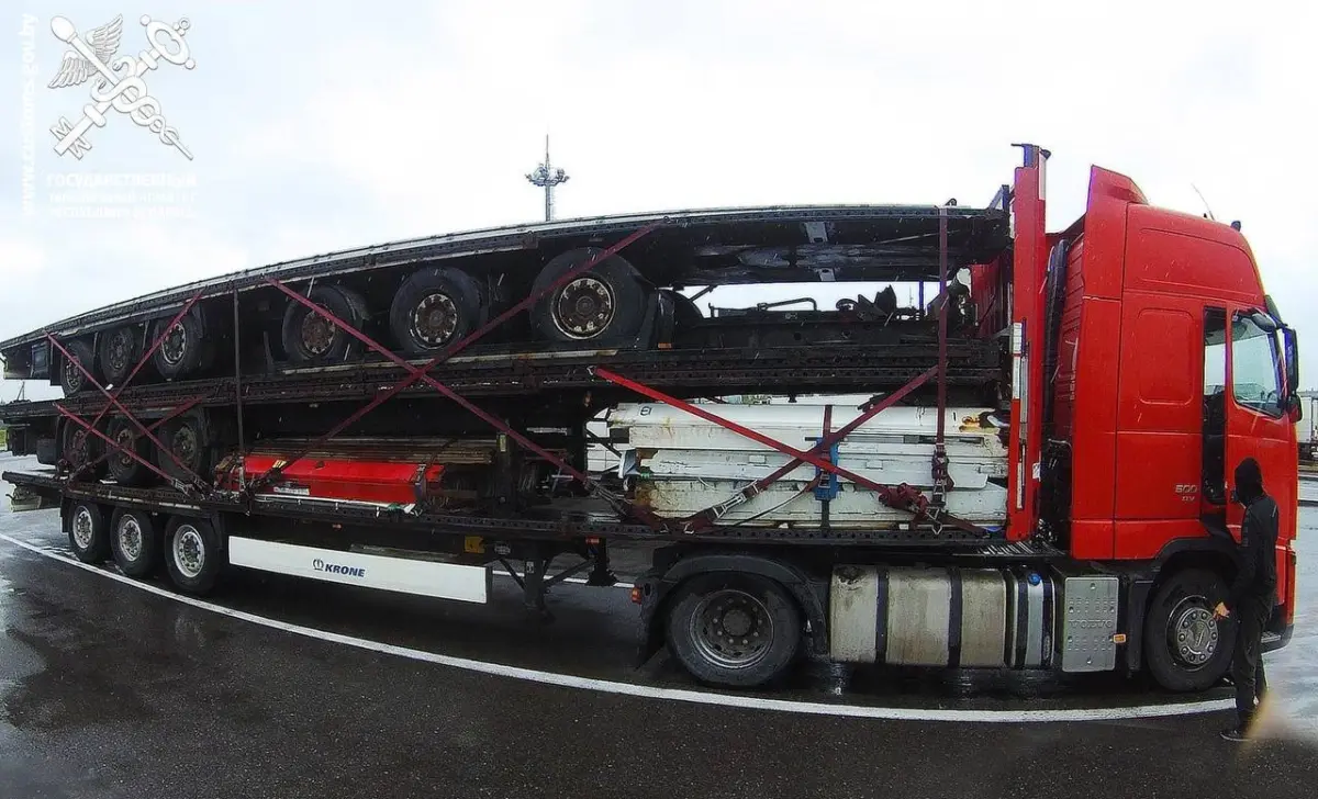 Красный тягач везёт на платформе несколько полуприцепов, закреплённых ремнями