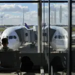 Пассажиры сидят у окна в аэропорту Варшавы, за стеклом – самолёты у трапов