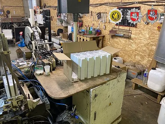 Помещение подпольной табачной фабрики с коробками сигарет на столе.