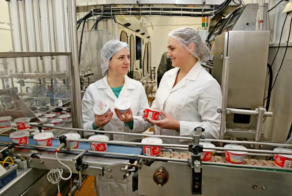 Сотрудницы в белых халатах и сетках на голове работают на молочном производстве