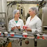 Сотрудницы в белых халатах и сетках на голове работают на молочном производстве