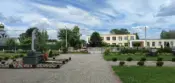 Площадка в центре Клейников с памятником, школой и благоустроенной территорией, на фоне зелени и голубого неба.