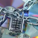 Цепи с кодовым замком, обвивающие компакт-диски и долларовые купюры, символизируют защиту авторских прав и ужесточение мер против нарушителей.