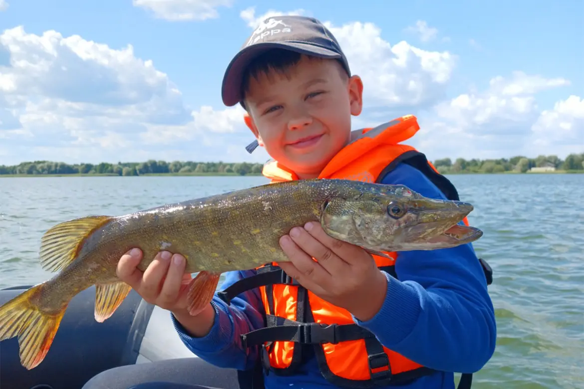 Мальчик в спасательном жилете держит щуку