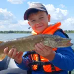 Мальчик в спасательном жилете держит щуку