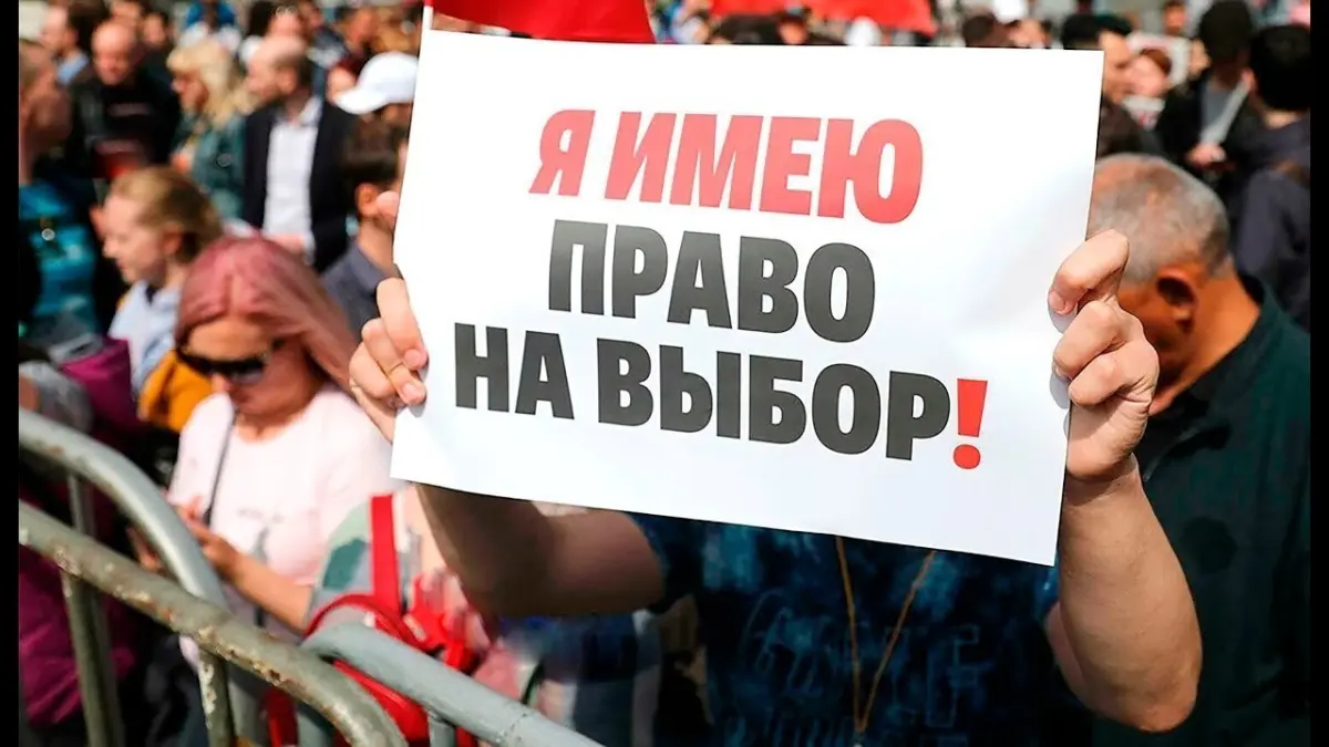 Человек держит плакат с надписью «Я имею право на выбор!» на фоне толпы на митинге.