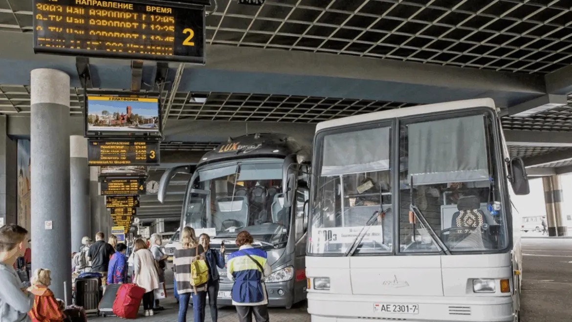 Минский автовокзал, автобусы на платформе и пассажиры с багажом в ожидании рейса в Вильнюс.