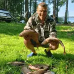 улыбающийся рыбак в камуфляжной куртке держит двух лещей