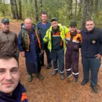 группа спасателей и найденный рыбак позируют для фото в лесу после завершения поисков*