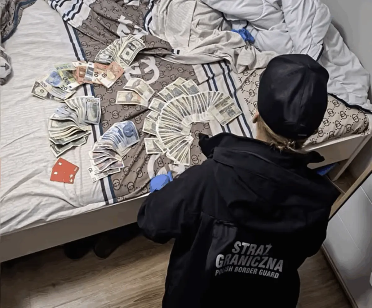 На кровати разложены пачки наличных в долларах, евро и злотых, сотрудник пограничной службы в форме фиксирует найденные средства.