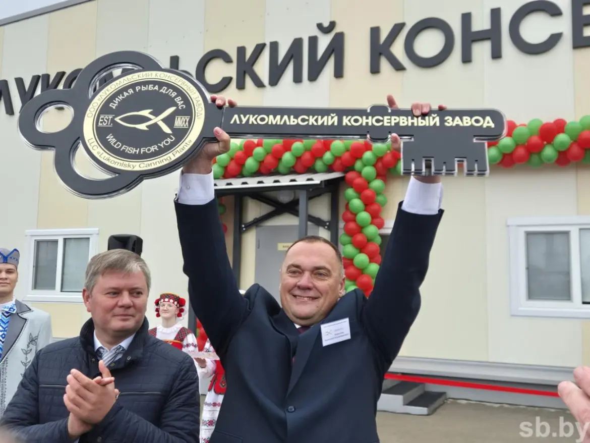 Мужчина поднимает символический ключ на открытии Лукомльского консервного завода
