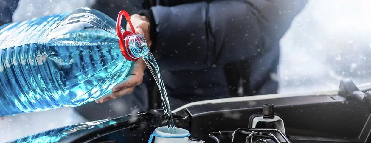 Крупная пластиковая канистра с синей незамерзающей жидкостью, которую заливают в подкапотное пространство автомобиля зимой.