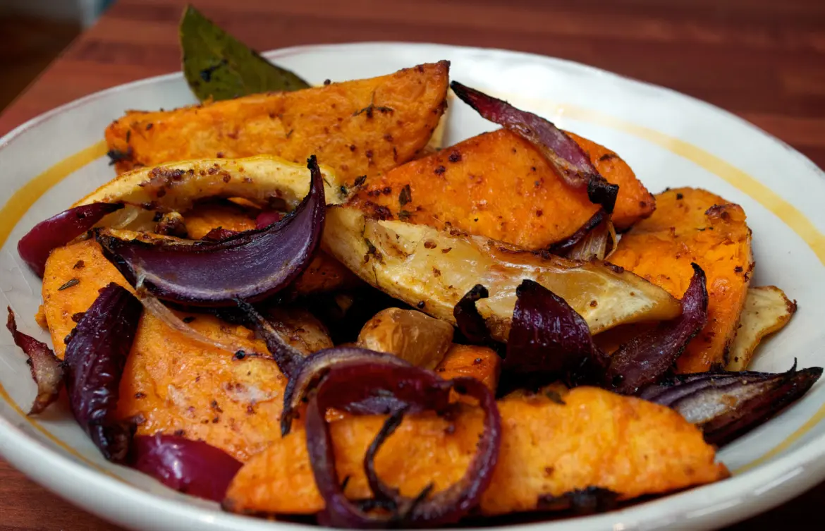 Дольки батата и лука, запечённые с приправами в глубокой миске.