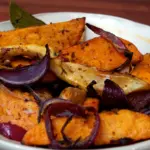 Дольки батата и лука, запечённые с приправами в глубокой миске.